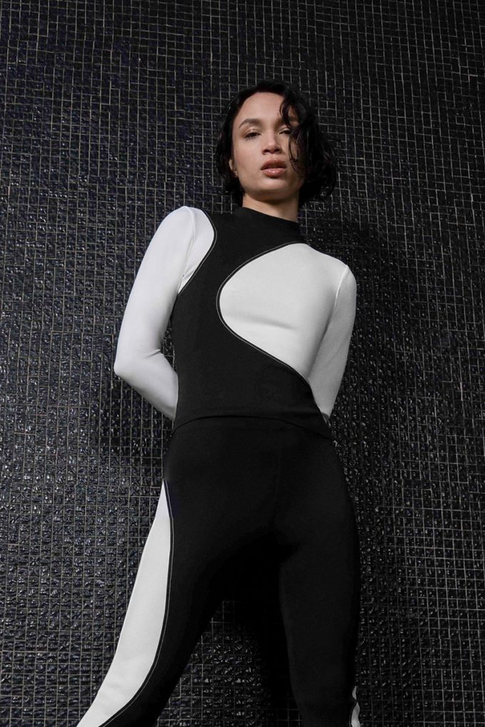 Le mannequin femme porte le top Lexi moulant à manches longues avec découpes organiques contrastées (noires et blanches) et surpiqûres associées au legging Lexi.